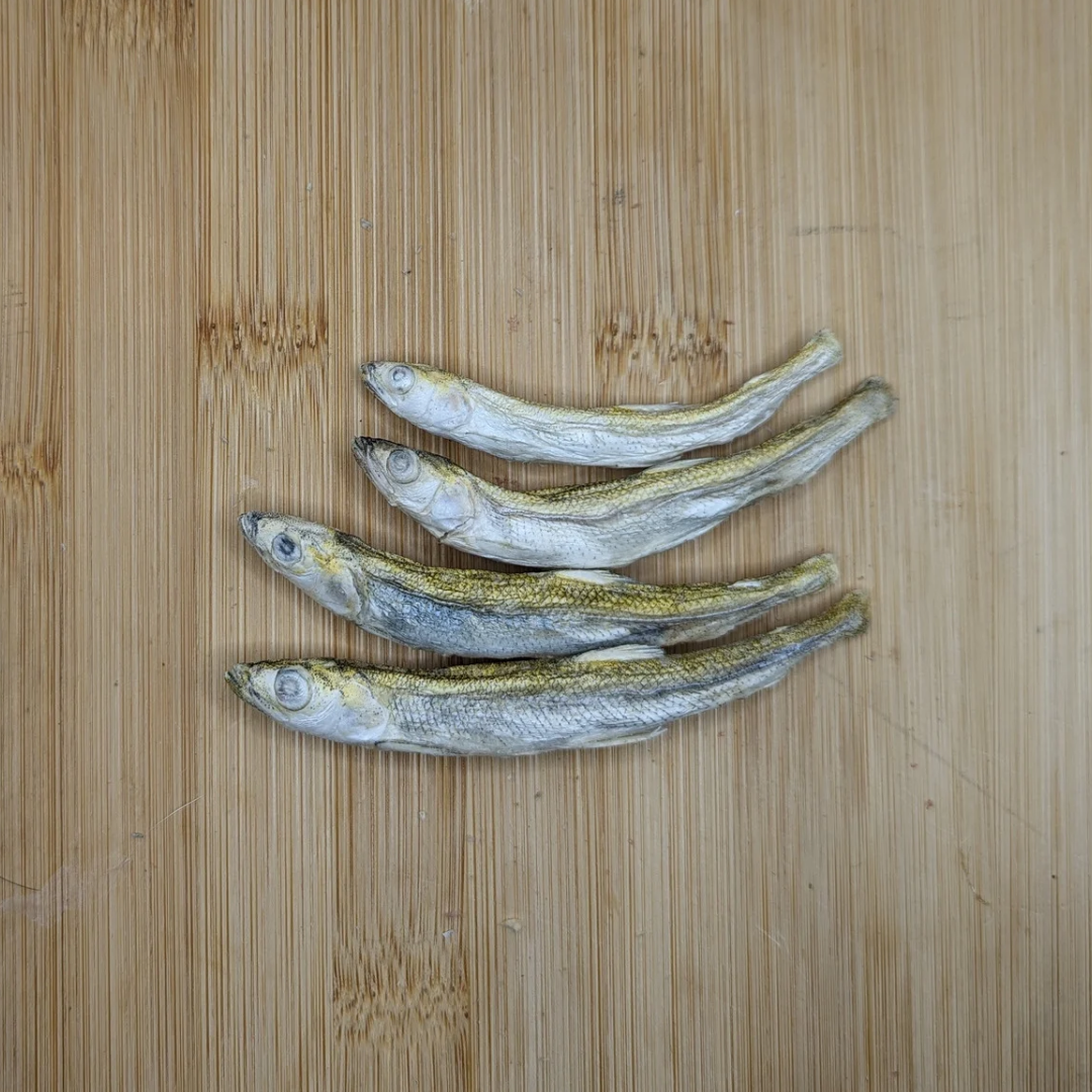 Four Beast Feast freeze-dried Smelt 1oz sitting on top of a wooden surface, their freeze-dried smelt bodies rich in Omega-3 fatty acids.