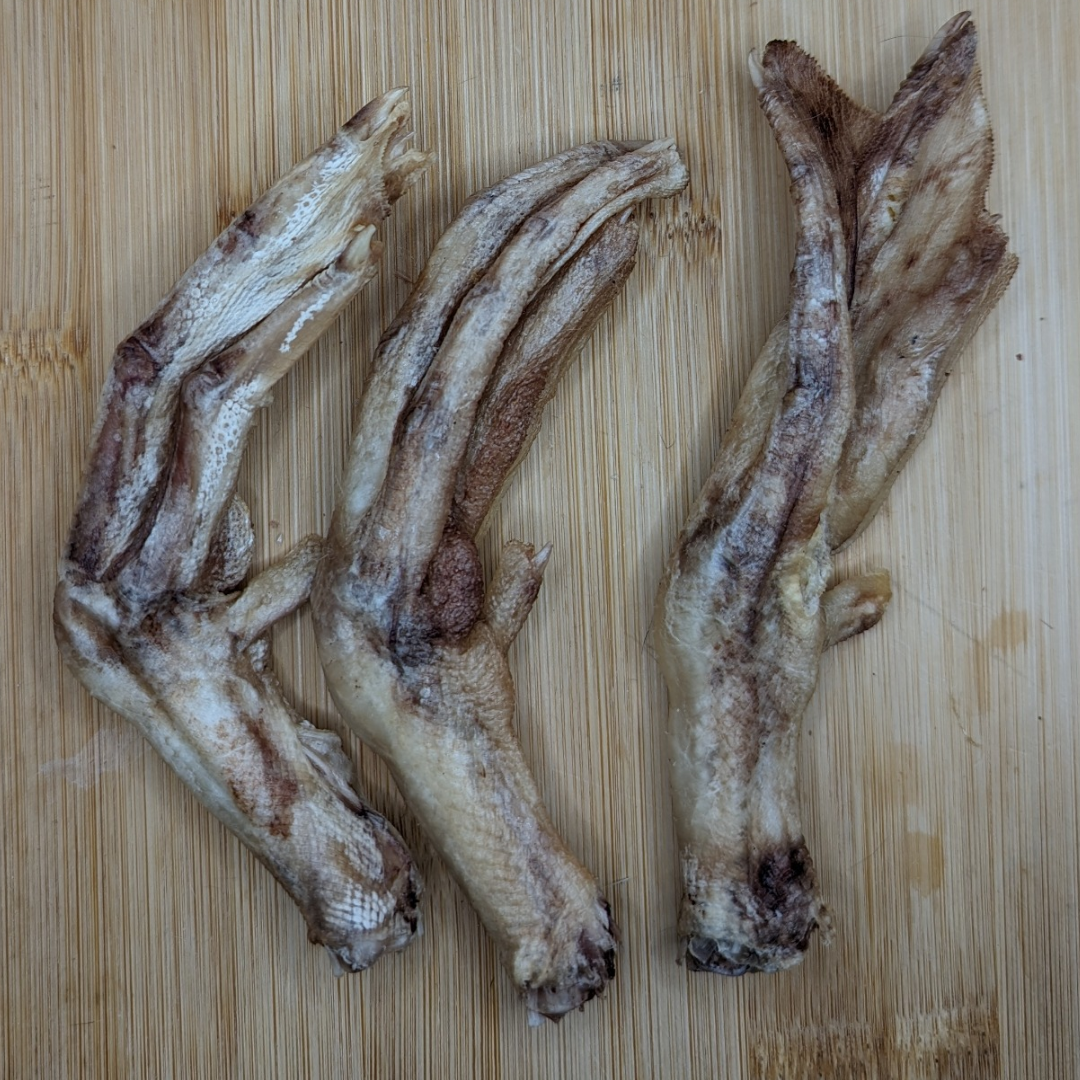 Three Freeze-Dried Duck Feet from Beast Feast on a wooden surface, beneficial for senior dogs with arthritis.