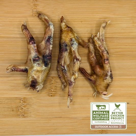 Three dehydrated chicken feet from Beast Feast on a wooden surface, with a "Certified Humane Raised" label indicating ethical standards.