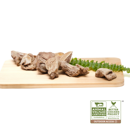 Cut dried mushrooms and Beast Feast freeze-dried chicken gizzards arranged on a wooden cutting board with a leafy green garnish, isolated on a white background.