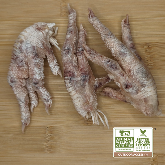 Three Beast Feast Freeze-Dried Chicken Feet on a wooden surface, certified by the Animal Welfare and Better Chicken Commitment with outdoor access.