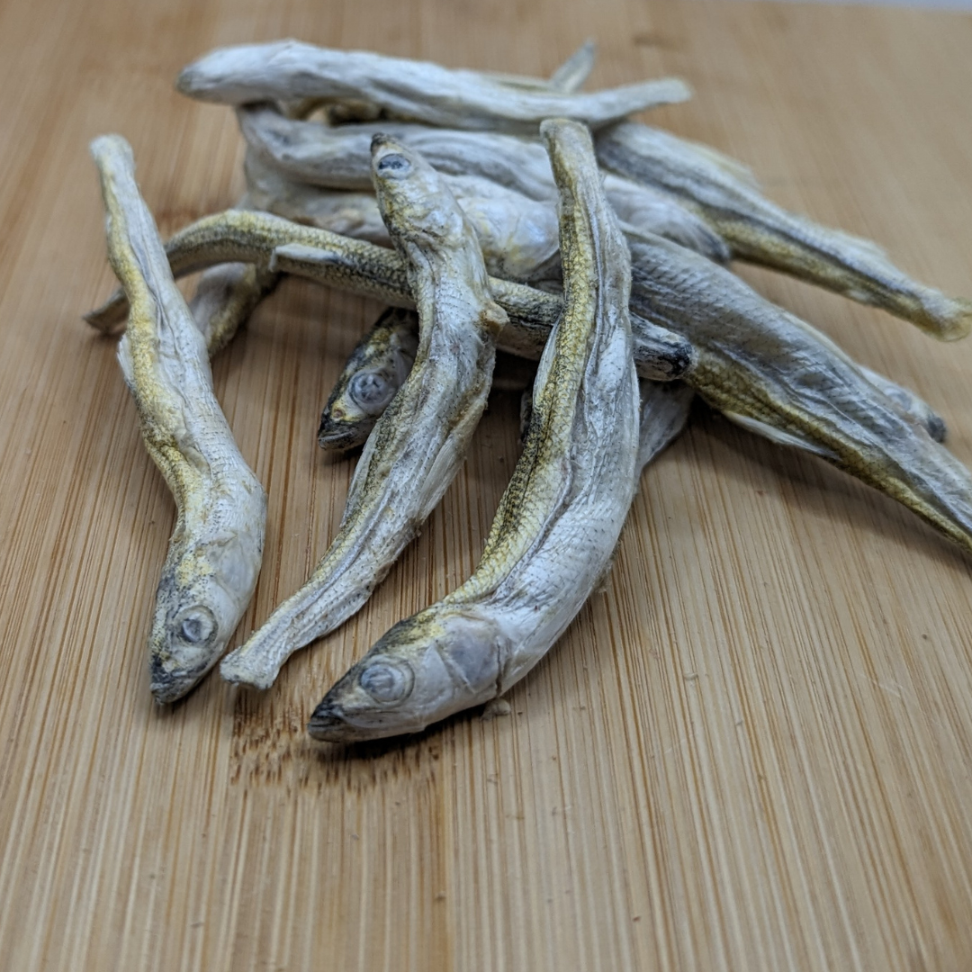 A sustainably wild-caught pile of Beast Feast Freeze-dried Smelt 1oz, rich in Omega-3 fatty acids, on a rustic wooden surface.