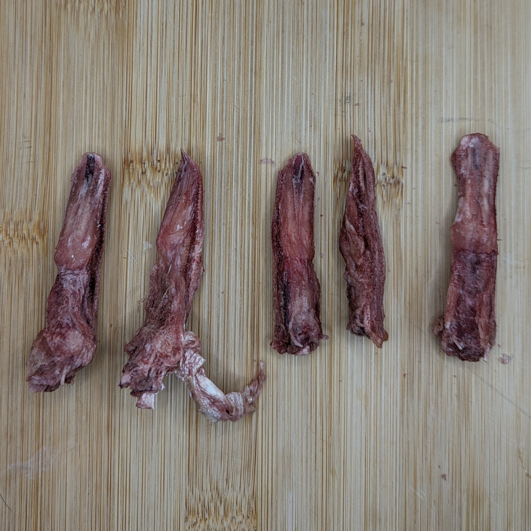 Five pieces of protein-rich Freeze-dried Duck Tongues 1oz, placed on a wooden cutting board.