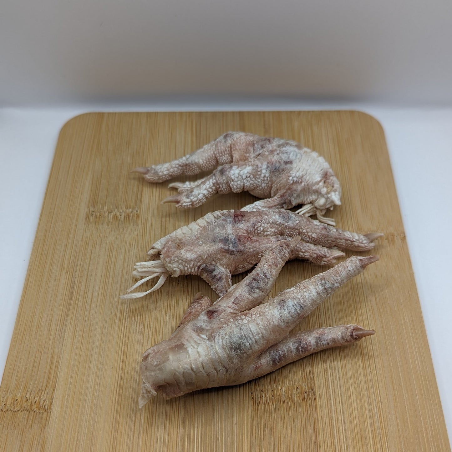 Three Freeze-Dried Chicken Feet from Beast Feast, adhering to the Better Chicken Commitment standards, on a wooden cutting board.