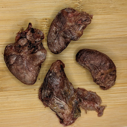 Four pieces of protein-rich Freeze-Dried Duck Hearts 1 oz from Beast Feast on a wooden surface.
