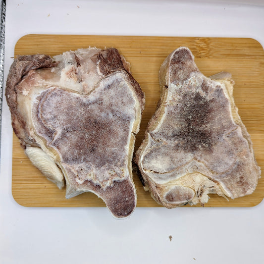 Two large, freeze-dried slices of Beast Feast Bison Knuckle on a wooden cutting board, showing frost and ice crystals covering the meat surfaces.